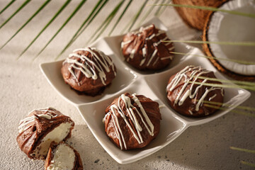 Chocolate profiteroles, eclairs, with coconut cream on a light background, on the background of green palm leaves