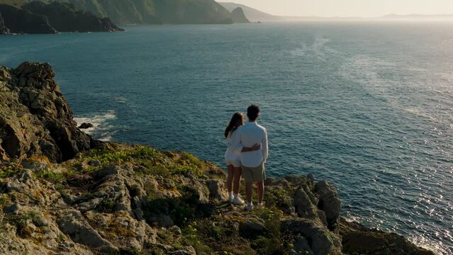 Couple Standing On Cliff Overlooking The Ocean On The Atlantic Coast Near Ferrol In A Coru&ntilde;a, Spain. aerial pullback