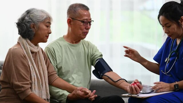 Female healthcare worker measuring arterial blood pressure elderly male during home visit. Elderly healthcare and hypertension concept