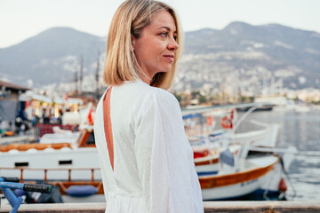 A profile of a pretty blonde woman. Boats, sea mountains on the background 