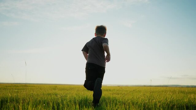 Boy Running In The Park. Happy Family A Kid Dream Concept. Child Son Boy 8 Years Old Running On Lifestyle The Grass In The Summer In The Park Rear View At Sunset. Kid Run In Nature