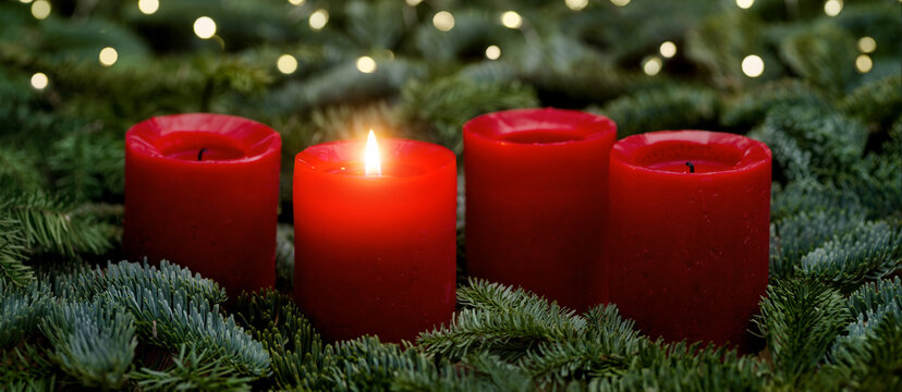 Red Advent candles, one burning, with fir branches and bokeh lights. The image is part of a set.
