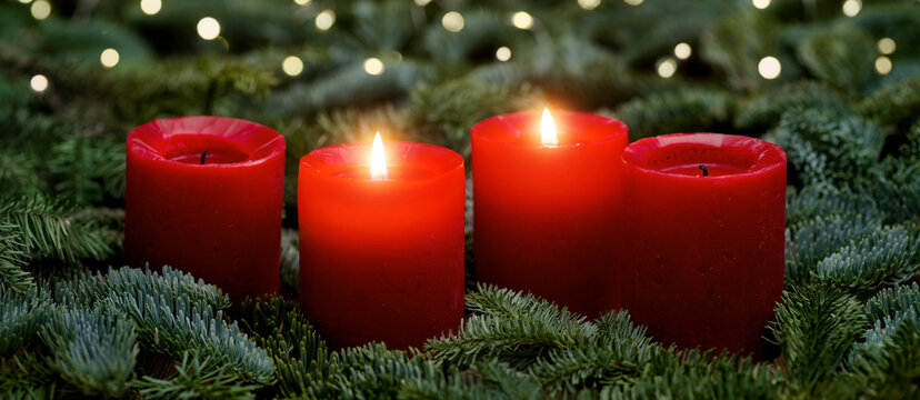 Red Advent candles, two burning, with fir branches and bokeh lights. The image is part of a set.