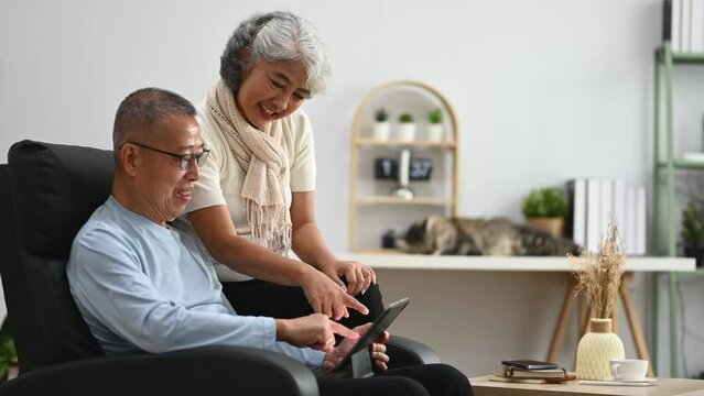 Cheerful senior couple using digital tablet scrolling, reading news feed in social media and browsing internet