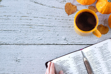 Hand holding open holy bible book of psalms with coffee cup, autumn leaves, and pumpkin on wooden table. Top view. copy space. Christian thanksgiving, biblical study, gratitude and praise concept. - Powered by Adobe