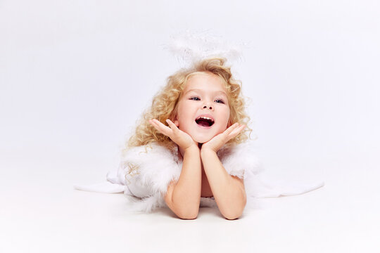 Happy, smiling, cute little girl child in white dress in image of angel standing isolated over white studio background. Concept of childhood, imagination, fantasy, fashion and beauty, holidays