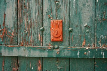 A bright orange lock in contrasted by an old wooden teal door that is weathering away. 
