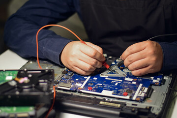 computer technician A laptop motherboard repairman is using an IC meter to find defects on the motherboard to repair on his table. Board repair using modern technology