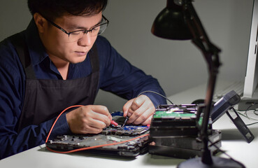 A young man who is a computer technician A laptop motherboard repairman is using an IC meter to find defects on the motherboard to repair on his table. Repair boards with technology