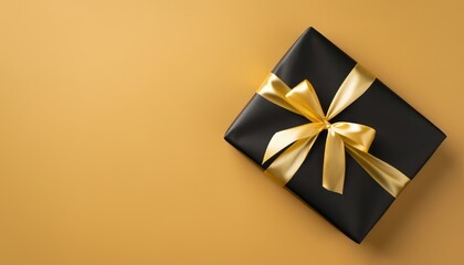Top view of black giftbox with gold ribbon on beige background with empty space