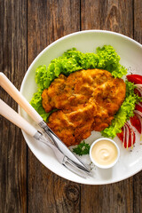 Crispy breaded seared chicken cutlet with lettuce and tomatoes on wooden table
