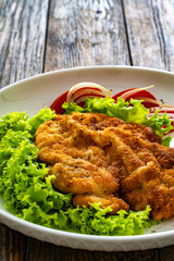 Crispy breaded seared chicken cutlet with lettuce and tomatoes on wooden table
