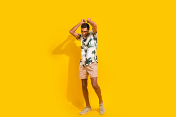 Full body photo of attractive young man dancing raise arms have fun dressed stylish palms print clothes isolated on yellow color background