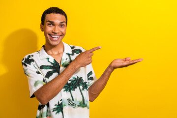 Portrait of impressed excited guy wear print clothes with ring in nose directing at empty space on arm isolated on yellow color background