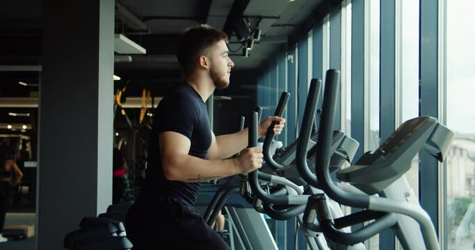 A close-up of a man's legs exercising on an orbitrek in the rays of the sun. Good atmosphere in the gym. High quality 4k footage