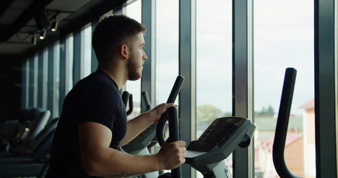 A close-up of a man's legs exercising on an orbitrek in the rays of the sun. Good atmosphere in the gym. High quality 4k footage