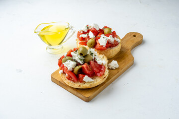 Greek dish dakos with ripe tomatoes, feta cheese, herbs and olive oil, lie on a wooden board, light...