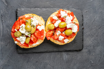 Bright appetizing appetizer dakos-Greek cuisine, bun with ripe tomatoes and feta cheese, dark background. View from above.