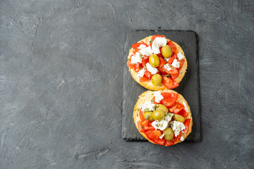 Dakos is a Greek dish with ripe and juicy tomatoes, feta cheese, olives, herbs, dark background. Top view, free space.