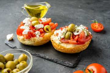 Dakos, Cretan dish with bread, tomatoes, butter, herbs and feta cheese or cottage cheese on a dark background.