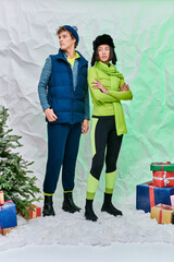 multiethnic couple in warm wear near gift boxes and Christmas tree on snow in studio, festive season