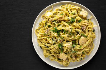 Homemade Creamy Chicken Bacon Pesto Pasta on a Plate on a black background, top view. Flat lay, overhead, from above. Copy space.