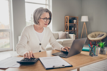 Photo of serious confident senior lady accountant dressed white cardigan counting bills modern...