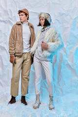 full length of interracial fashion models in cold-weather wear posing on white crumpled backdrop