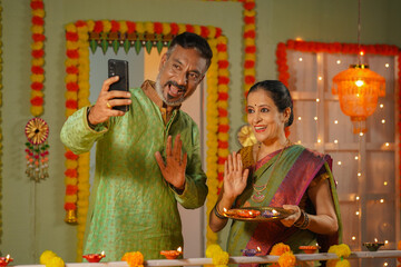 Senior couple speaking on video call using smartphone during diwali festival celebration at home - concept of family bonding, traditional culture and Technology