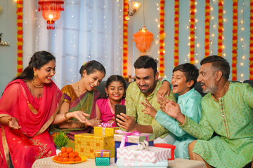 Group of happy indian joint family seeing mobile phone during family diwali festival celebration - concept of emotional reunions, Relationship bonding and social media sharing