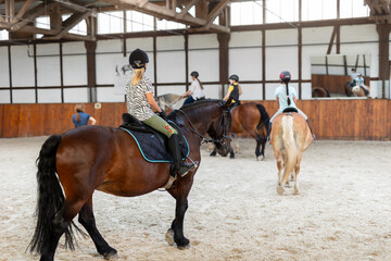 Horse riding school. Little children girls at group training equestrian lessons in indoor ranch...