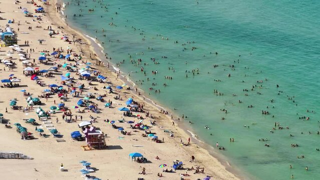 Crowded South beach in Miami, USA. Many people enjoying vacations time swimming in ocean water and relaxing on warm Florida sun