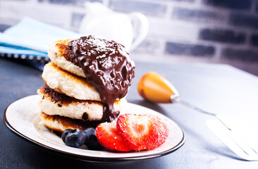 Traditional syrniki served with fresh strawberries, blueberry, mint leaves, drizzled with chocolate