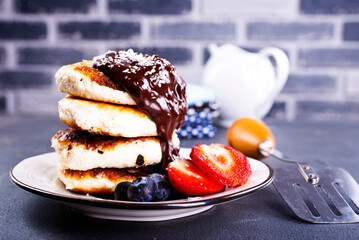 Traditional syrniki served with fresh strawberries, blueberry, mint leaves, drizzled with chocolate