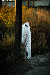 A man dressed as a ghost from a white sheet is hiding behind a post by the road. Ghost Challend 2021. Halloween Celebration. Spooky season.