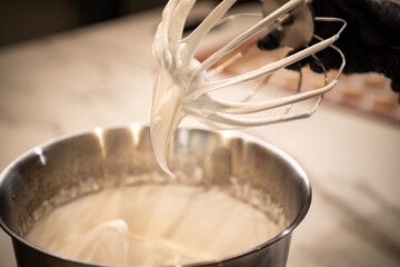 Hand holding a mixing whisk near the mixer bowl, preparing heavy cream and cheese. close up, front...
