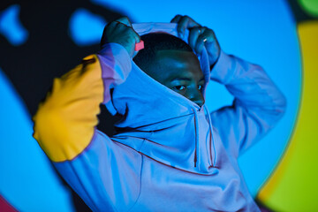 good looking young man posing while putting on hood in digital projector lights, fashion concept