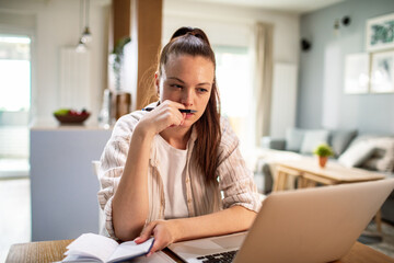 Young woman going over her bills and payments on the laptop at home - obrazy, fototapety, plakaty