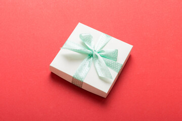 wrapped Christmas or other holiday handmade present in white paper with green ribbon on colored background. Present box, decoration of gift on colored table, top view with copy space