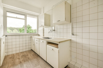 Fototapeta na wymiar a kitchen with white tiles on the walls and wood flooring in front of the window looking out to the trees outside
