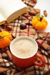 A cup of coffee with autumn decoration and book on blanket. Cozy home, autumn concept.