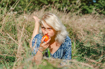 Cute blonde woman lying in grass eating apple at picnic
