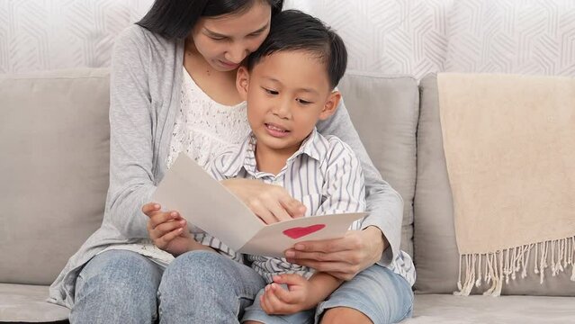 Asian single mom getting present from kid happy mom enjoy reading handmade love card from small son She hug kiss little child on mother day valentine or birthday Love and care in fa