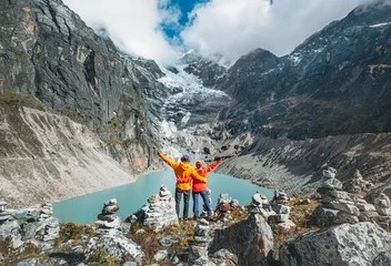 Photo sur Plexiglas Makalu Couple trekkers dressed bright jackets on the rock enjoying a glacier falling in high altitude Sabai Tso glacial lake cca 4350m. Makalu Barun National Park, Mera peak climbing route, Nepal.