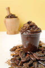 Hard chocolate in a plastic cup and in the background a mortar full of chocolate grains