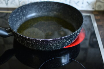 vegetable oil in a frying pan on a black electric stove - obrazy, fototapety, plakaty