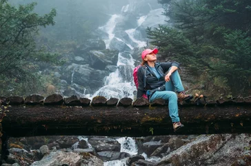 Store enrouleur occultant sans perçage Makalu Young woman with backpack sitting on a wooden bridge and enjoying of power mountain river waterfall during Makalu Barun National Park trek in Nepal. Mountain hiking and active people concept image.