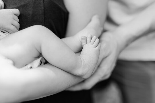 A newborn feet and legs are held in her father's hands in black and white