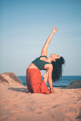 Woman doing Yoga exercises on the sandy beach with the sea in the background