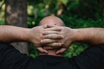View from behind of mature man with little hair or alopecia with his hands on the nape of his neck....